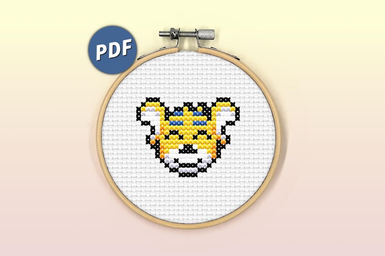 May include: A cross-stitch pattern of a yellow tiger face with blue eyes, in a wooden embroidery hoop.