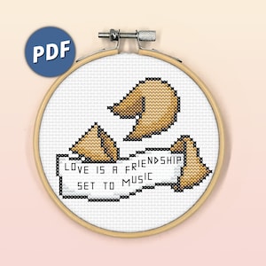 May include: A cross-stitch pattern featuring three fortune cookies and a white banner with the text "Love is a friendship set to music".