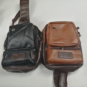 May include: Two leather crossbody bags, one black and one brown. Both bags have a flap closure with a buckle and a zipped pocket on the front. The bags also have a zipped pocket on the back.