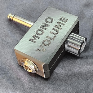 May include: A black 3D printed box with the words "MONO VOLUME" printed on the top. The box has a knob on the right side and a 1/4 inch jack on the left side. A 1/4 inch plug is connected to the box.
