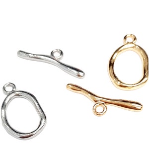 May include: Four metal jewellery findings in silver and gold tones. Two are open circles and two are curved bars with a loop at one end.