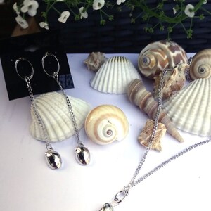 May include: A silver necklace and earrings set with a seashell pendant and matching earrings. The necklace and earrings are on a white background with seashells.