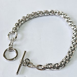 May include: A silver chain bracelet with a toggle clasp. The chain is made of a braided design.