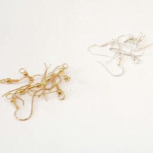 May include: A close-up of two sets of earring findings. One set is gold and the other is silver. The gold findings have a small ball at the end of the wire.