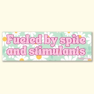 Può includere: Uno striscione verde chiaro con margherite bianche e testo rosa che recita "Fueled by spite and stimulants". Il testo è in uno stile di font retrò. Lo striscione ha un bordo bianco e un piccolo logo in basso a destra che recita "Philly Frogs".