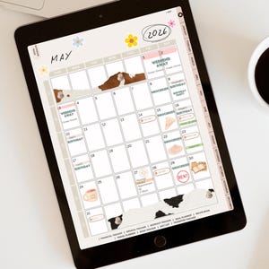 May include: A digital planner displayed on a tablet screen, featuring a May 2026 calendar layout. The planner includes decorative elements like floral accents and cow print details. A cup of coffee and a stylus are also visible.