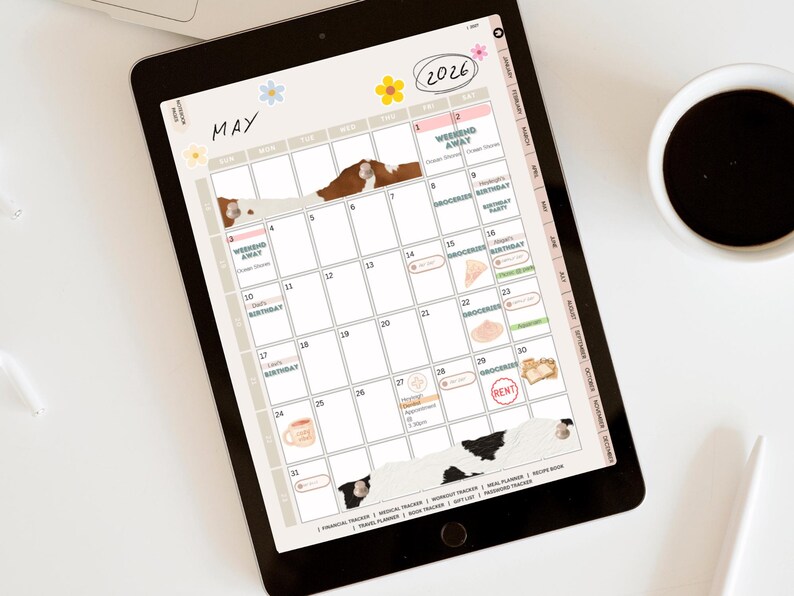 May include: A digital planner displayed on a tablet screen, featuring a May 2026 calendar layout. The planner includes decorative elements like floral accents and cow print details. A cup of coffee and a stylus are also visible.