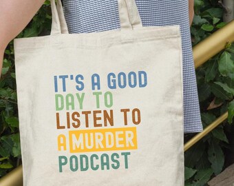 May include: A white canvas tote bag with the text "It's a good day to listen to a murder podcast" in colorful letters.