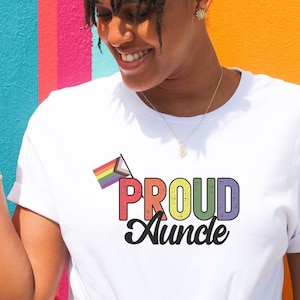 May include: White t-shirt with a rainbow pride flag and the text "PROUD  Auncle" in colorful, distressed lettering.