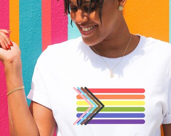 May include: A white t-shirt with a rainbow flag design featuring a black and brown arrow pointing to the right. The flag has six stripes in the colors of red, orange, yellow, green, blue, and purple.
