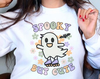 May include: White sweatshirt with a graphic of a ghost wearing roller skates and the text "Spooky But Cute" in colorful letters surrounded by flowers.