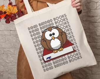 May include: A white tote bag with the text "Read Banned Books" repeated multiple times. A cartoon owl is sitting on a red book with the text "Read Banned Books" on the front of the bag.