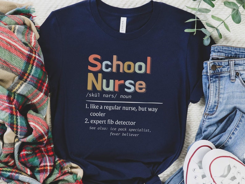 Peut inclure: Un t-shirt bleu marine avec le texte "School Nurse" en lettres color&eacute;es. Le texte est d&eacute;fini comme "comme une infirmi&egrave;re ordinaire, mais bien plus cool" et "d&eacute;tecteur de mensonges expert".
