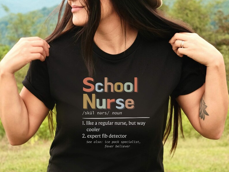 Peut inclure: Un t-shirt noir avec le texte "School Nurse" en lettres color&eacute;es. Le texte est d&eacute;fini comme "comme une infirmi&egrave;re ordinaire, mais bien plus cool" et "d&eacute;tecteur de mensonges expert".