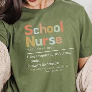 Peut inclure: T-shirt vert avec le texte "School Nurse" d&eacute;fini comme "comme une infirmi&egrave;re ordinaire, mais bien plus cool" et "d&eacute;tecteur de mensonges expert".