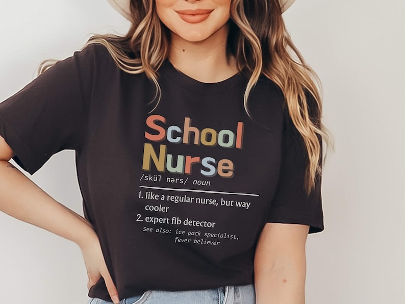 Peut inclure: Un t-shirt noir avec le texte "School Nurse" en lettres color&eacute;es. Le texte est d&eacute;fini comme "comme une infirmi&egrave;re ordinaire, mais bien plus cool" et "d&eacute;tecteur de mensonges expert".