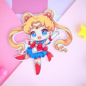 May include: A cartoon sticker of Sailor Moon in her iconic pose, with a blue and red sailor uniform, yellow hair, and a red bow. The sticker is on a pink background.