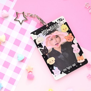 May include: A clear plastic ID card holder with the text "MY BIAS" and "my only one". The card features a photo of a person making a heart shape with their hands, surrounded by cartoon animal illustrations. A silver star keychain is attached.