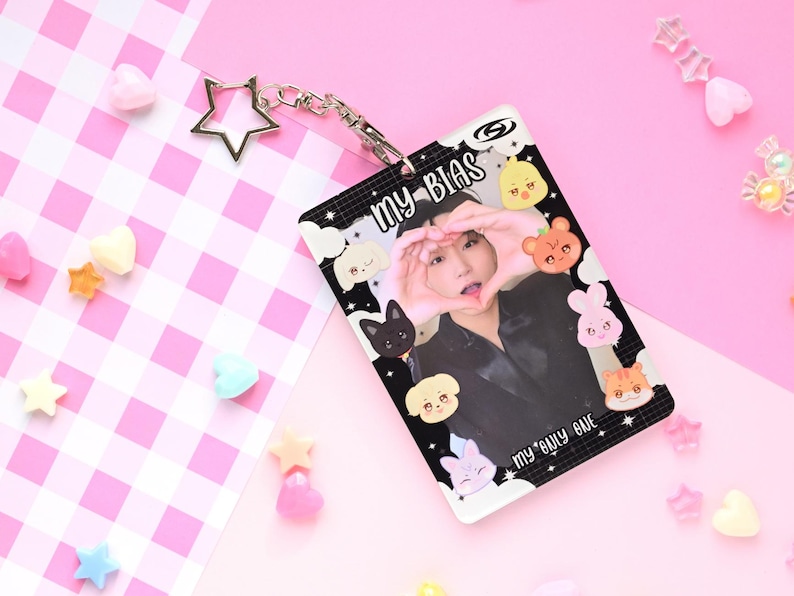May include: A clear plastic ID card holder with the text "MY BIAS" and "my only one". The card features a photo of a person making a heart shape with their hands, surrounded by cartoon animal illustrations. A silver star keychain is attached.