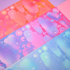 May include: Three sheets of colorful stickers with a galaxy theme. The stickers feature clouds, stars, and flowers in shades of pink, blue, and purple.