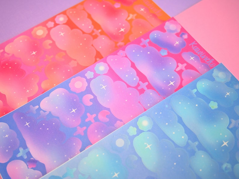 May include: Three sheets of colorful stickers with a galaxy theme. The stickers feature clouds, stars, and flowers in shades of pink, blue, and purple.
