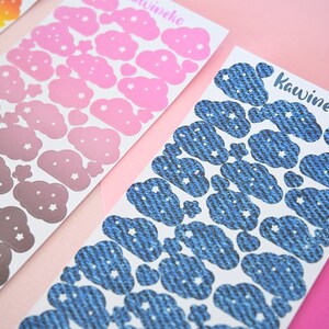 May include: Three sheets of stickers with cloud designs. The first sheet has pink clouds with white stars, the second sheet has gray clouds with white stars, and the third sheet has blue denim-textured clouds with white stars. The text "Kawineko" is printed on the third sheet.