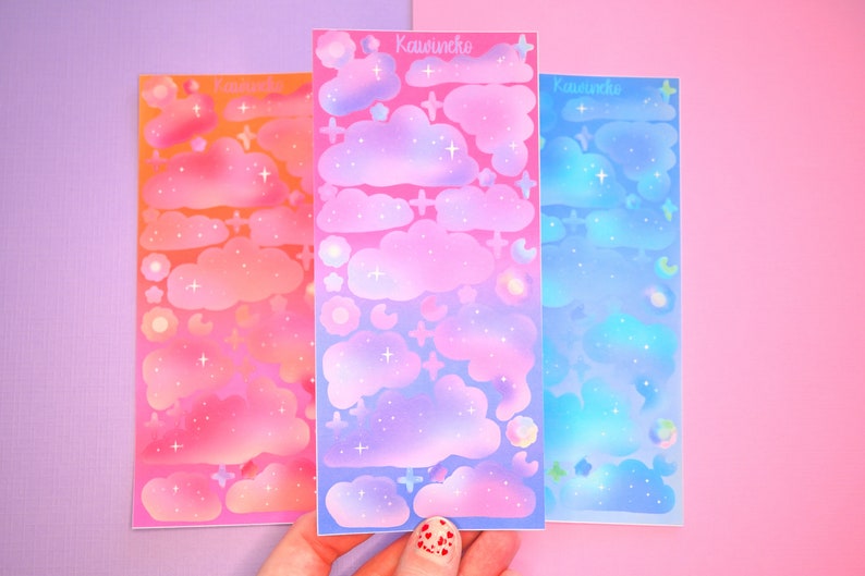 May include: Three sheets of colorful cloud stickers with a gradient background. The stickers are pink, purple, and blue with white stars and clouds. The text "Kawaii.nko" is printed on each sheet.