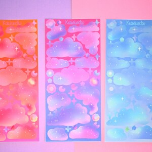 May include: Three sheets of holographic stickers featuring clouds, stars, and moons in a gradient of pink, purple, and blue. The stickers are labeled "Kawuneche".