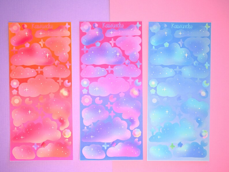 May include: Three sheets of holographic stickers featuring clouds, stars, and moons in a gradient of pink, purple, and blue. The stickers are labeled "Kawuneche".