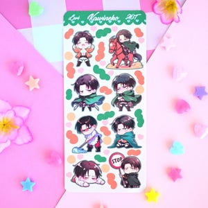 Op de afbeelding: Een vel met stickers met een cartoonfiguur met verschillende gezichtsuitdrukkingen. Het figuur draagt een groene mantel en heeft bruin haar. De stickers zijn op een witte achtergrond met kleurrijke accenten. De tekst "Levi Kawineko 2017" staat bovenaan het vel.