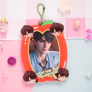 May include: An apple-shaped acrylic charm featuring a portrait of a person in a blue suit, surrounded by cartoon character illustrations. The charm has a green loop for hanging and the text "What was that Pip-Squeak?!"