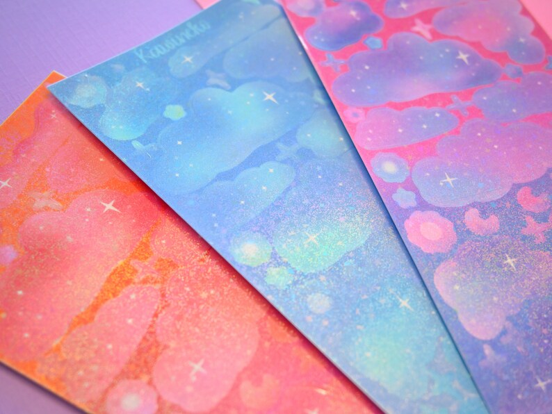 May include: Four sheets of iridescent holographic sticker paper with a cloud and star design. The sheets are in shades of blue, pink, orange, and purple.