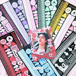 May include: A set of colorful sticker sheets with various designs, including arrows, hearts, caution signs, and the text "Kawineko". The stickers are on a black background and have a glossy finish.