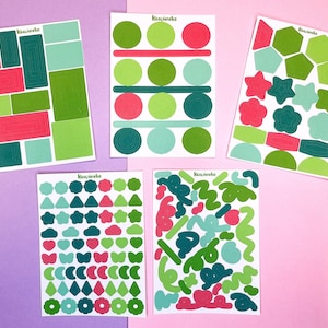 May include: Four sheets of colourful stickers with various shapes and designs. The stickers are green, red, and blue. The stickers are on a pink and purple background.