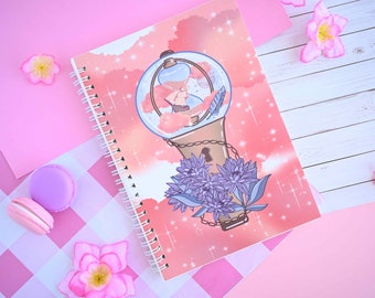 May include: A pink spiral bound notebook with a colorful illustration of a glass orb with a keyhole and a chain. The orb is surrounded by clouds and purple flowers. The background is a pink and white checkered pattern.