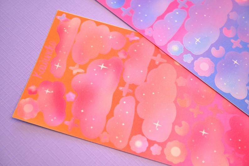May include: Two sheets of stickers with a celestial theme. The stickers are pink, orange, and blue with white stars and clouds. The text "Kawaii" is printed on one sheet.