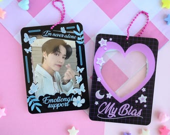 May include: Two black photo card holders with pink chain straps. One features a photo of a person with the text "I'm never alone" and "Emotional support". The other has a heart-shaped frame and the text "My Bias".