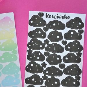 May include: Two sheets of stickers featuring black clouds with white stars. The sheet on the right has the text "Kawineko" in black cursive lettering.