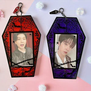Pode incluir: Dois porta-retratos de acrílico em formato de caixão com molduras pretas decoradas com teias de aranha, aranhas e morcegos. O suporte esquerdo é vermelho e o direito é roxo. Cada um inclui um pequeno pingente de caixão.