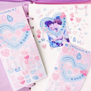 May include: Three sheets of stickers with a pastel pink and blue color scheme. Each sheet features a large heart with a watercolor effect and a variety of smaller hearts, stars, butterflies, and flowers. The text "KawaiiNeko" appears on two of the sheets.