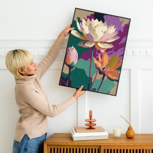 May include: A framed print of a floral illustration featuring three pink, white, and orange lotus flowers with green leaves on a purple and teal background.