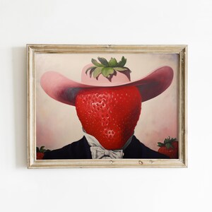 Peut inclure: Une impression d'art encadr&eacute;e repr&eacute;sentant le portrait surr&eacute;aliste d'une grosse fraise rouge portant un chapeau rose &agrave; larges bords et une veste de costume sombre avec une chemise blanche &agrave; col et un n&oelig;ud papillon. Deux fraises sont visibles.