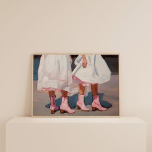 May include: Painting of two people wearing white dresses and pink boots. The painting is framed in a wooden frame.