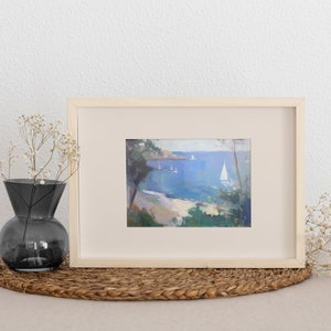 May include: A framed painting of a seascape with a sailboat in the distance. The painting is in a light wood frame and is set on a woven mat.