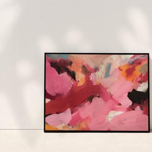 May include: Abstract art print in a black frame. The artwork features a vibrant mix of colors, including shades of pink, red, orange, and black. The brushstrokes create a dynamic and textured appearance, suitable for home decor.