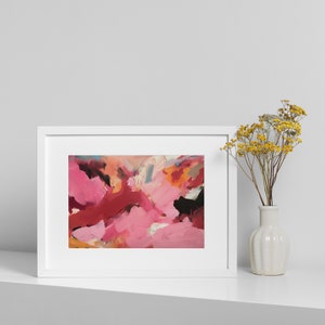 May include: Abstract art print in a white frame. The artwork features a vibrant mix of pink, red, and black brushstrokes. A small white vase with yellow flowers is placed to the right of the framed art, creating a balanced composition.