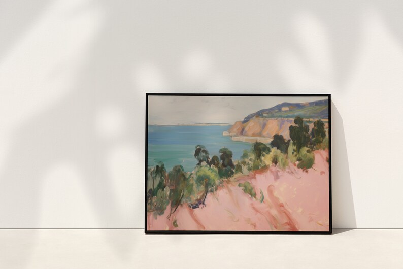 May include: A framed landscape painting featuring a coastal scene with a pink foreground, green trees, and a blue ocean meeting a distant cliffside under a pale sky. The artwork is enclosed in a thin black frame, displaying expressive brushstrokes.