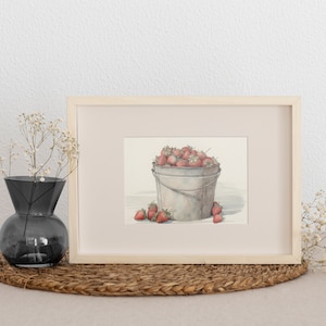 May include: A framed watercolor painting of a metal bucket filled with red strawberries. The bucket is sitting on a white surface. The painting is framed in a light wood frame.