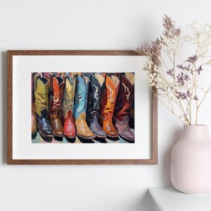 May include: A framed art print featuring a row of colorful cowboy boots in shades of yellow, orange, red, blue, and brown. The boots are depicted with detailed stitching and pointed toes, arranged side-by-side in a vibrant, painterly style.