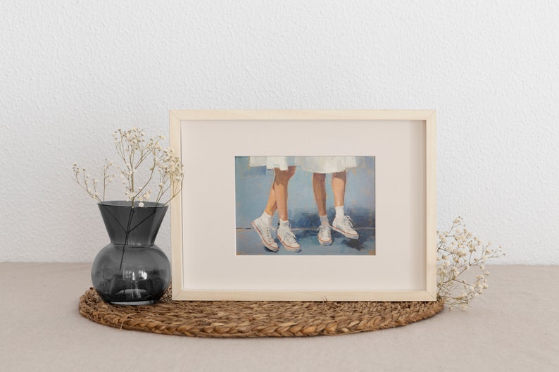 May include: A framed painting depicting two pairs of legs wearing white trainers. The legs are painted in a realistic style with a soft, muted colour palette. The background is a light blue.